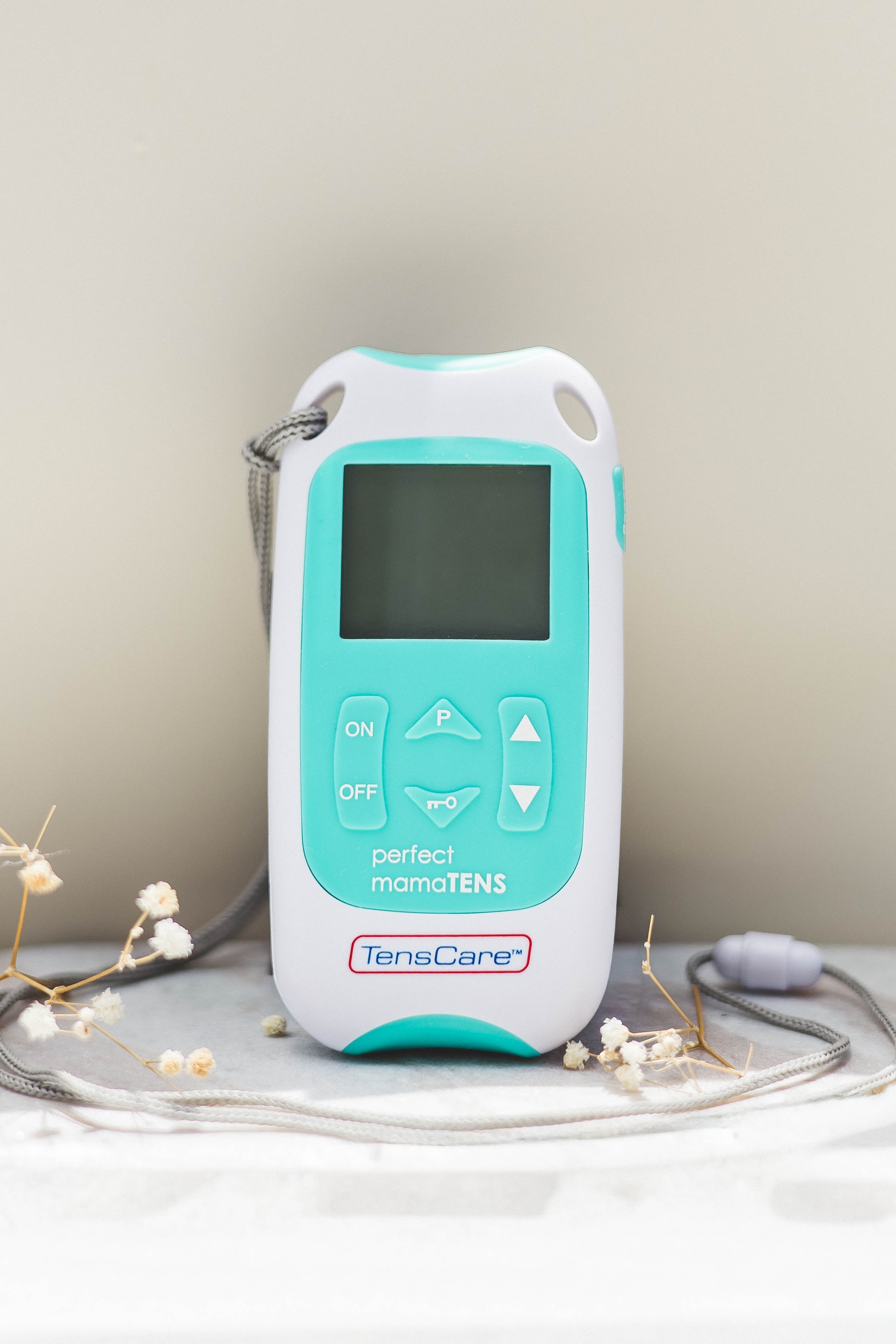 Aqua and White TENS machine device with some dried flowers around it for decoration