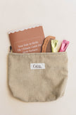 Beige corduroy pouch with a birth partner guide, birth comb, and other items on a light beige background