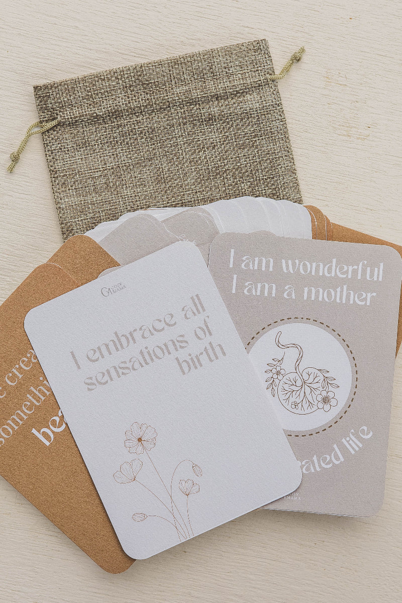 Set of birth affirmation cards with motivational phrases and a drawstring bag on a light wooden surface