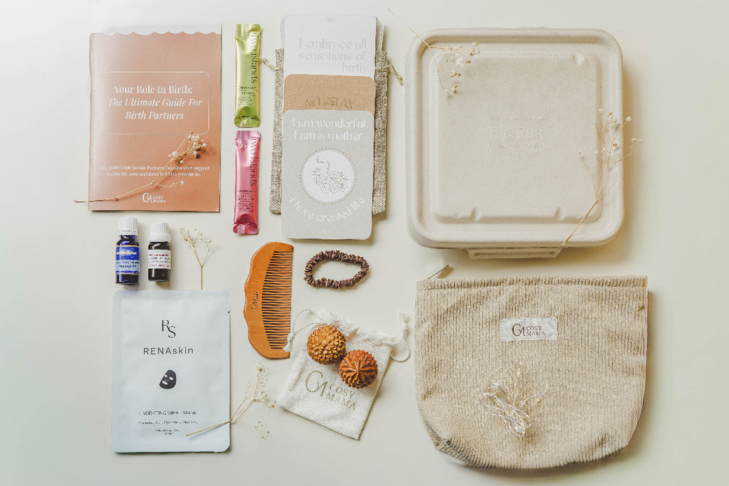 Entire Nurtured Birth Bundle from Cosy Mama on a beige background. The range includes a beige placenta container, birth affirmation cards, electrolyte sachets, birth orbs -spikey wooden balls, wooden birth comb, fairy lights, massage oil, face mask and silk hair tie.