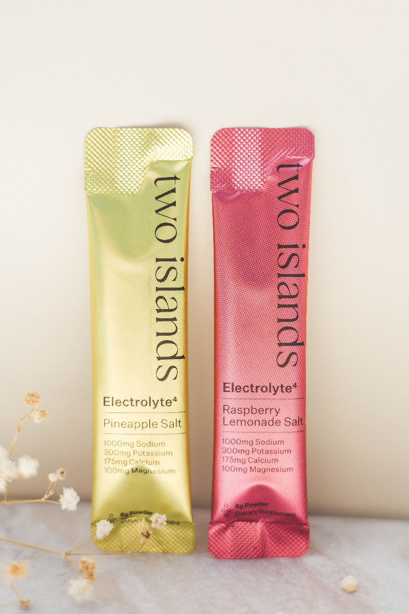 Two packets of 'two islands' electrolyte drinks, one pineapple salt and one raspberry lemonade salt, on a light background.