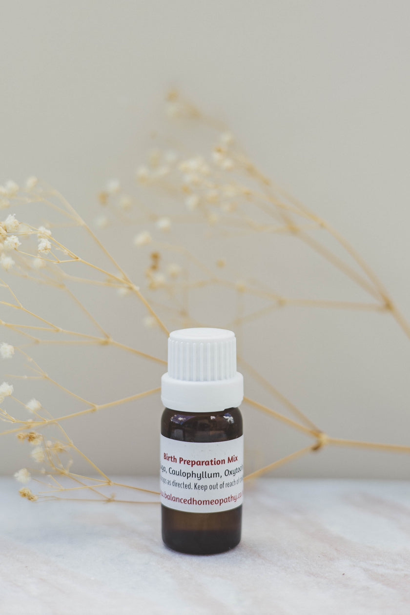 Small brown  amber bottle with a white cap on a light surface with dried plants in the background. Birth Mix