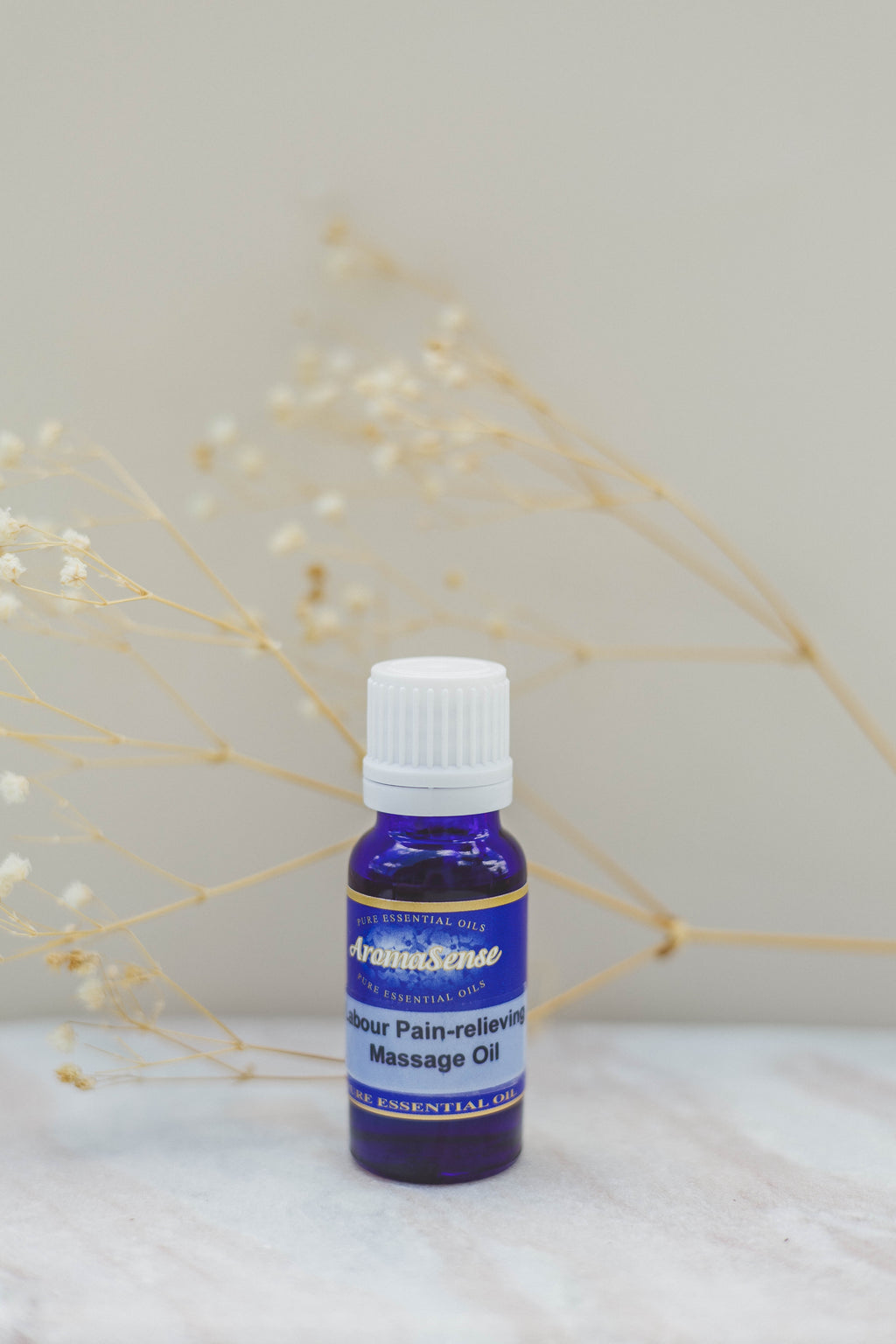 Bottle of AromaSense labour massage oil on a white surface with dried flowers in the background