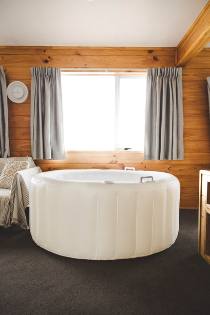 White freestanding birth pool in a room with wooden walls and a window where the curtains are open.