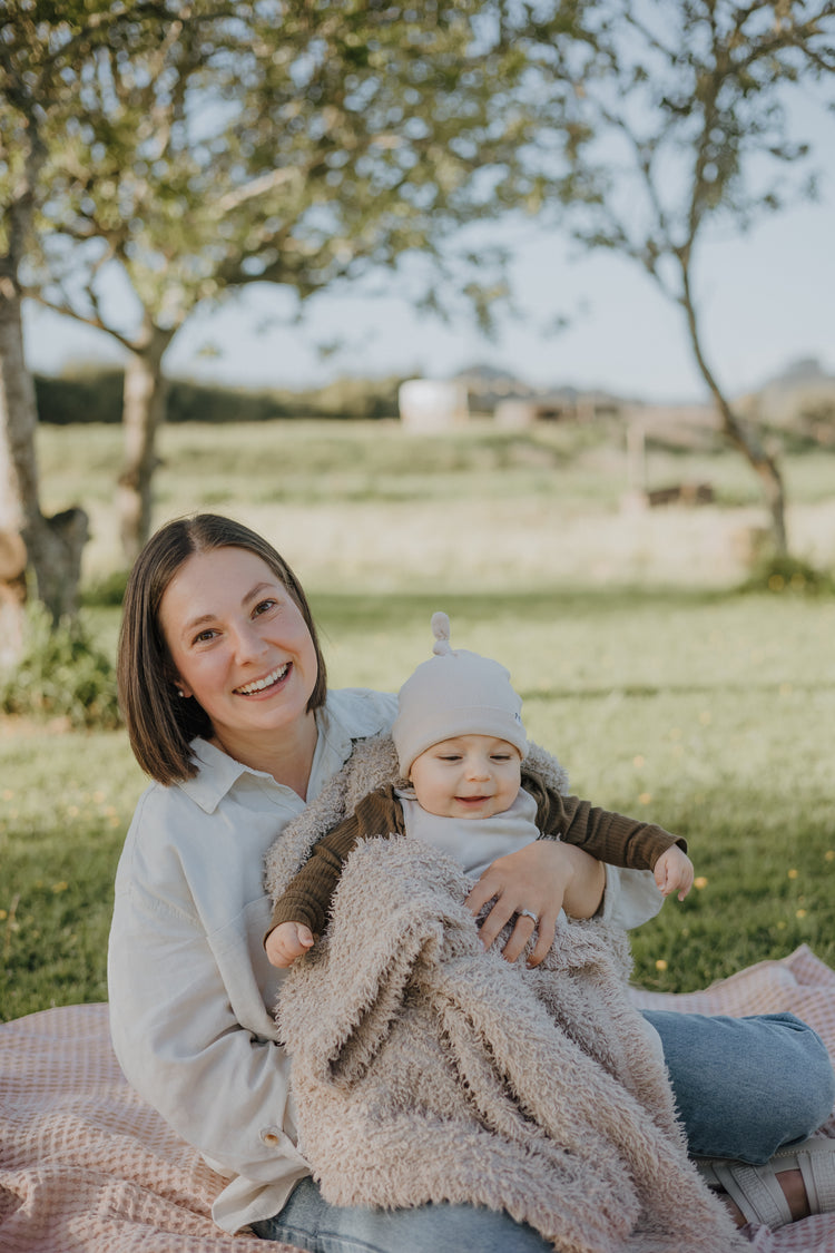 Woman holding a baby outdoors on a blanket with trees and grass in the background