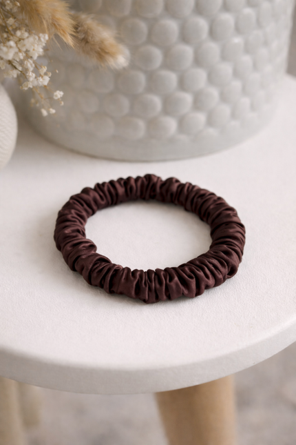 mulberry silk scrunchie on a white stand, with a plant pot in background